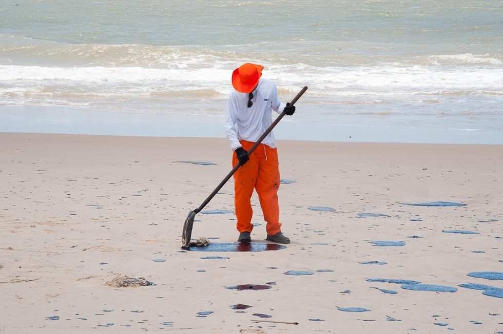 Homem tentando remover resíduos de petróleo de uma praia